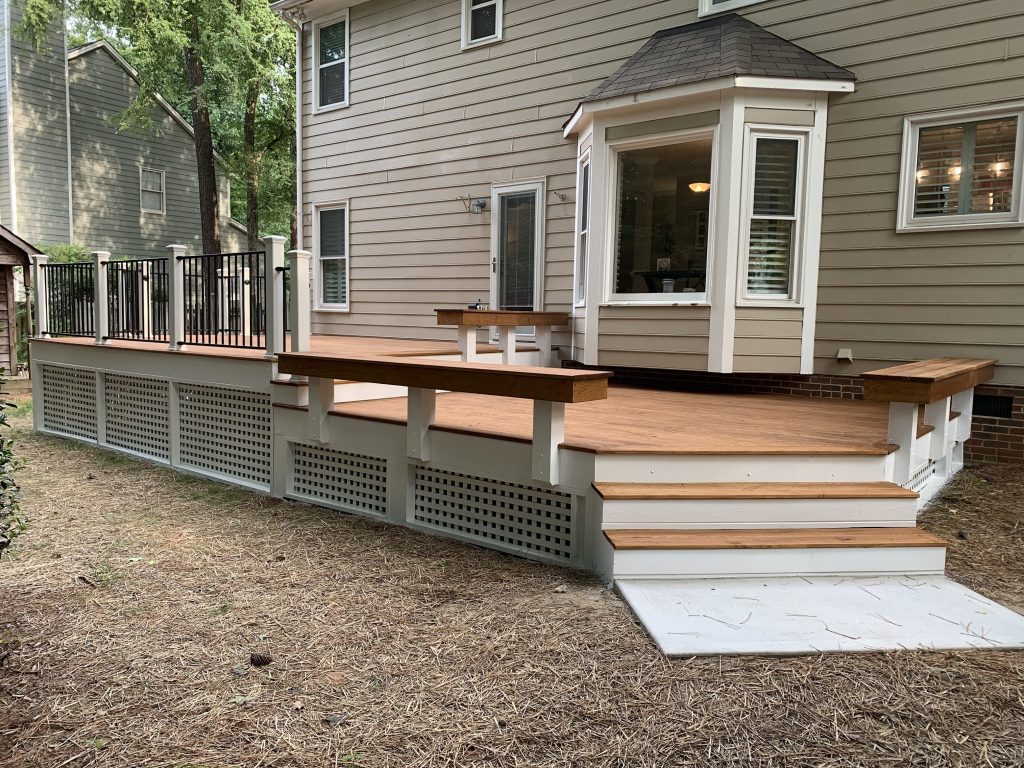 Photograph of a recently constructed outdoor deck. The deck features a beautifully stained wooden floor and is bordered by a sleek black metal railing. Post lights illuminate the space, adding a warm and inviting ambiance